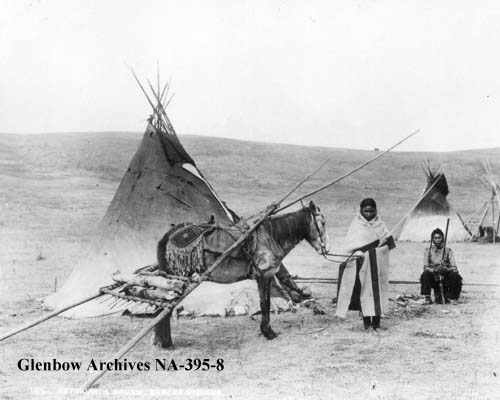 Astokumi or Crow Collar and wife, Sarcee, with their horse-drawn travois.