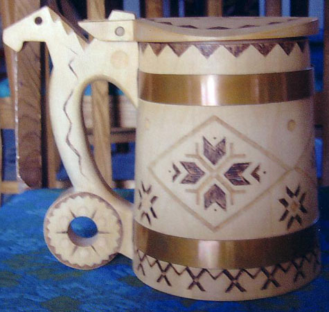 A simple beer stein is embellished with Estonian patterns burned on  wood. The handle is in the shape of a horse\'s head-a familiar design found on Estonian beer tankards. Crafted in the 1970s by Galena Koddo.