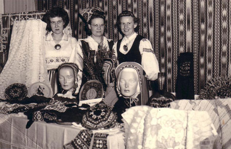 Three Calgary Estonians, dressed in national costume, with a display of Estonian handicrafts, 1953.
