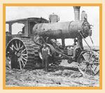 Two people are dwarfed by a steam traction engine on a farm near Cereal in 1914. This is an Avery undermounted engine so no stress from the engine (bottom) is put on the engine (top).